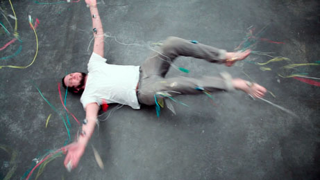 Man laying on asphalt with strings floating in the air.