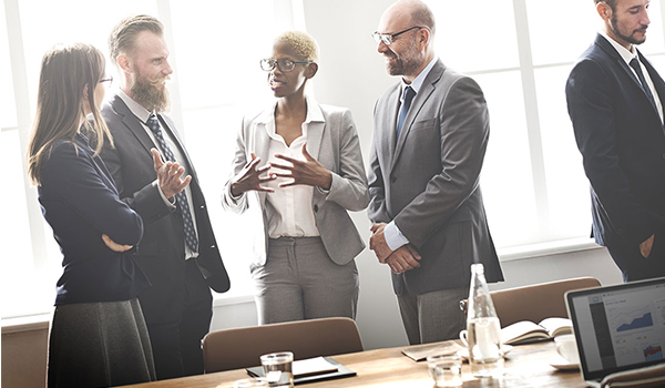 group of professionals standing by conference table talking in a group of four