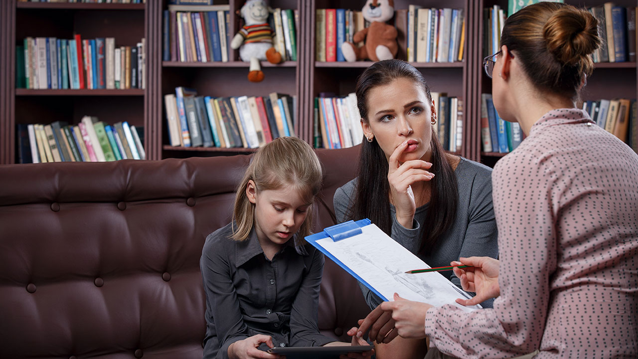 Female holding clipboard and sitting with a mother and yound daughter.