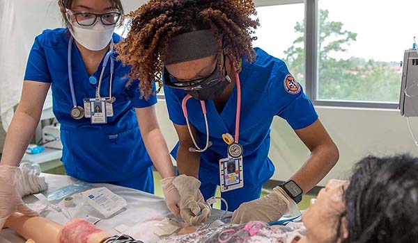 Two nursing students practicing on a dummy.