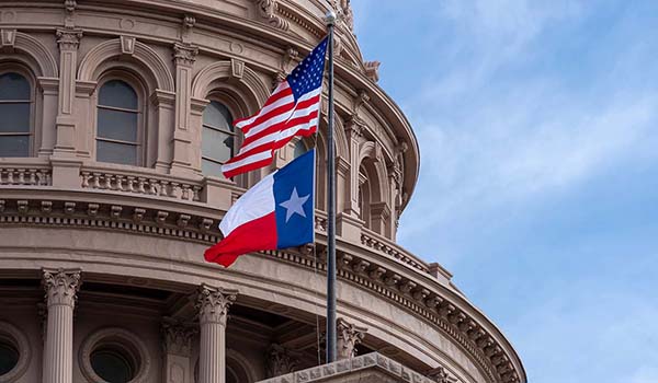 The American and Texas flag flying over the Texas Capitol.