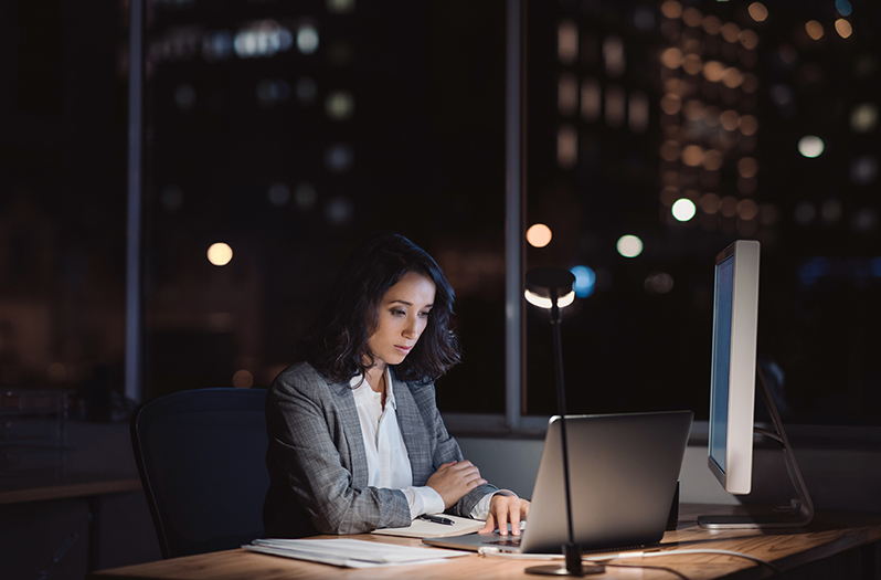 Woman sitting in office on laptop. She is illuminated by her laptop screen.