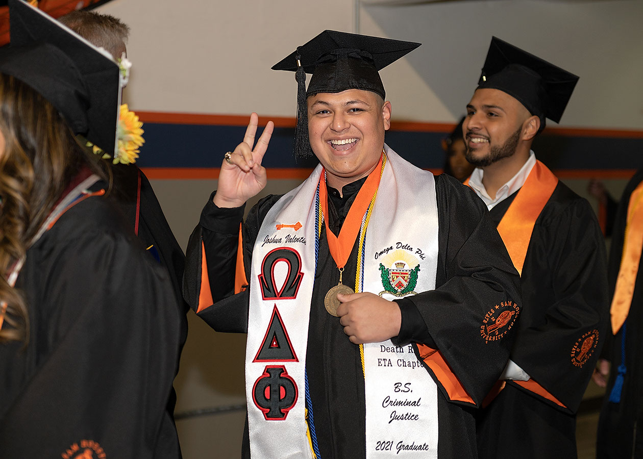 A graduate flashes the peace sign as he enters the coliseum.