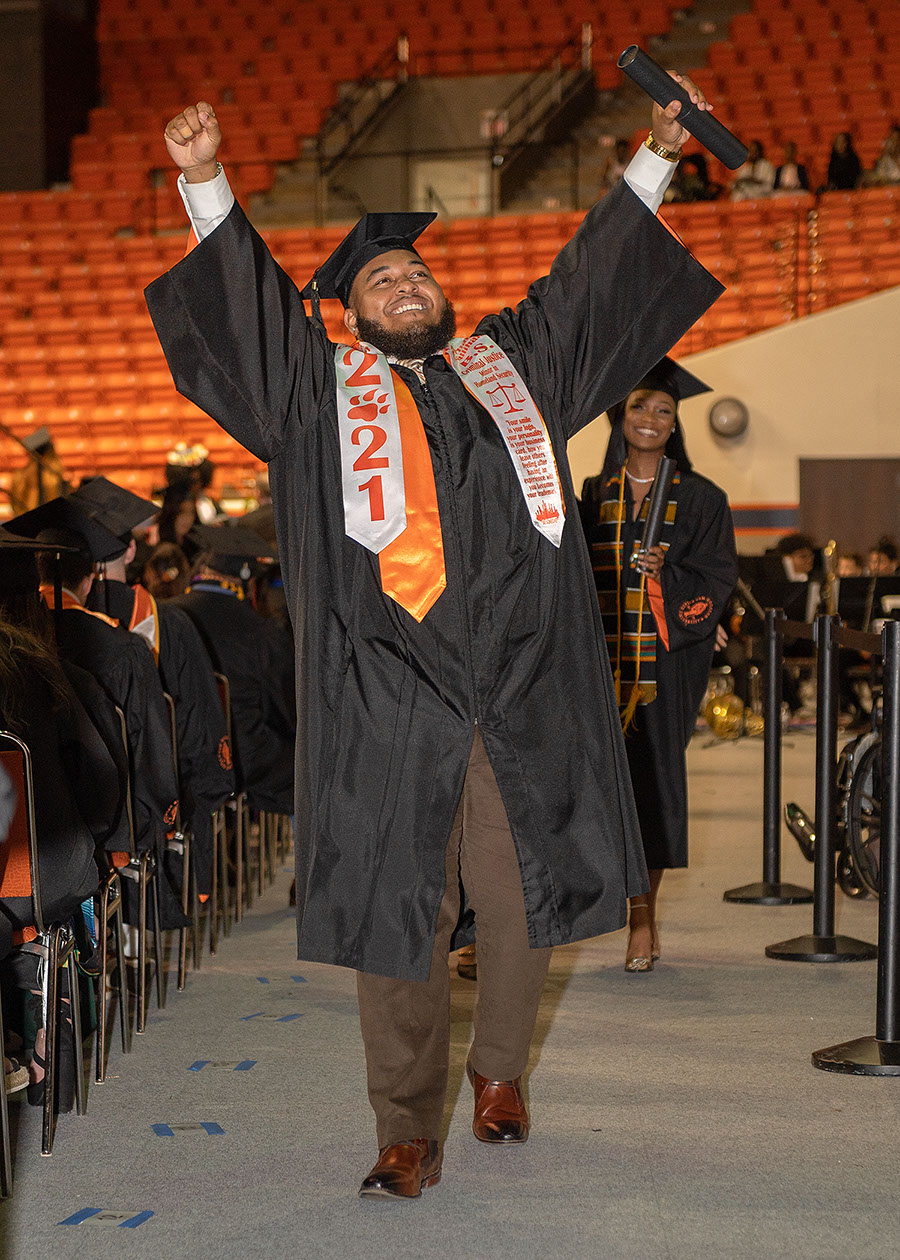 A graduate raises his hands in triumph and smiles at the audience after accepting his degree on stage.