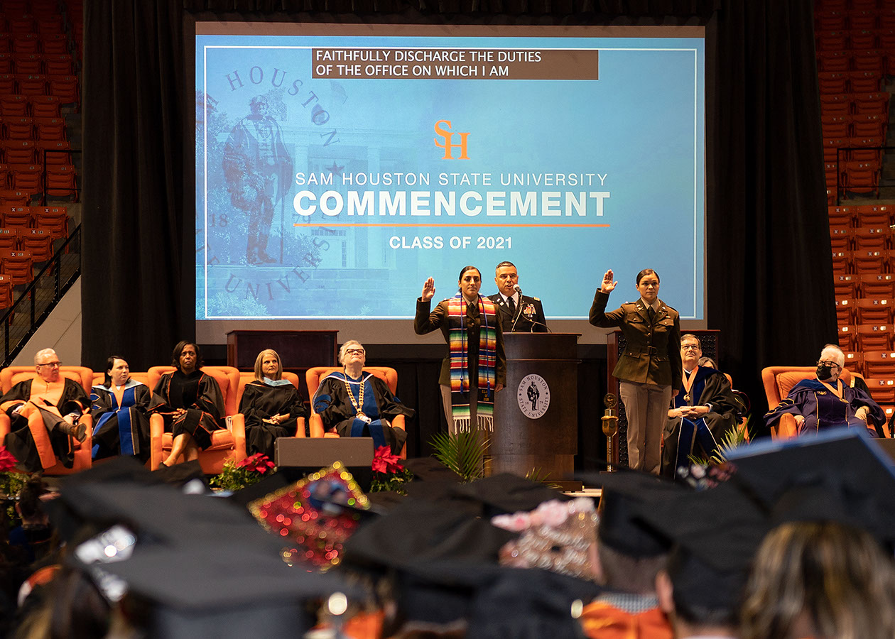 A graduate raises his hands in triumph and smiles at the audience after accepting his degree on stage.