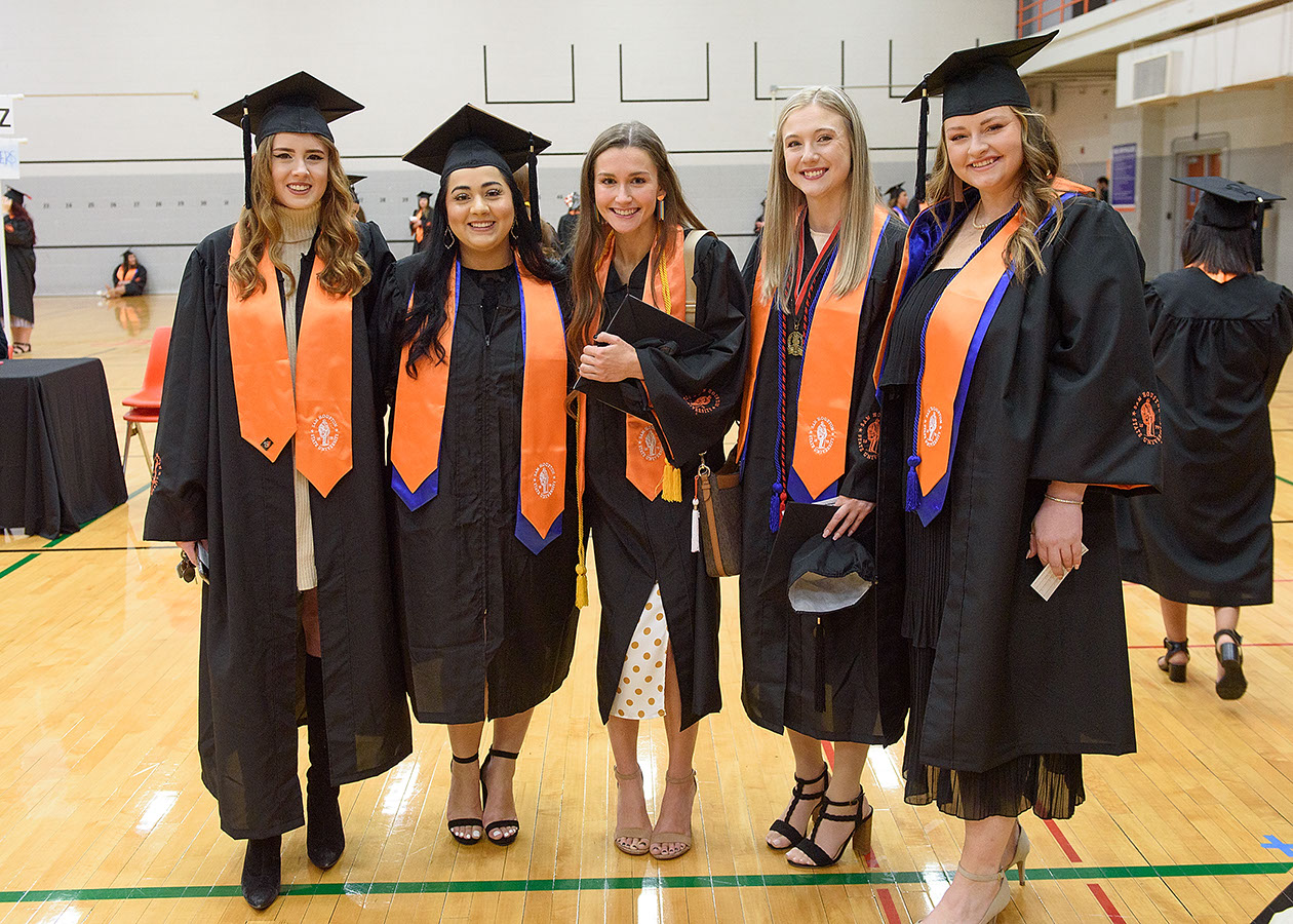 Five graduates pose with big smiles for the camera before their commencement ceremony.