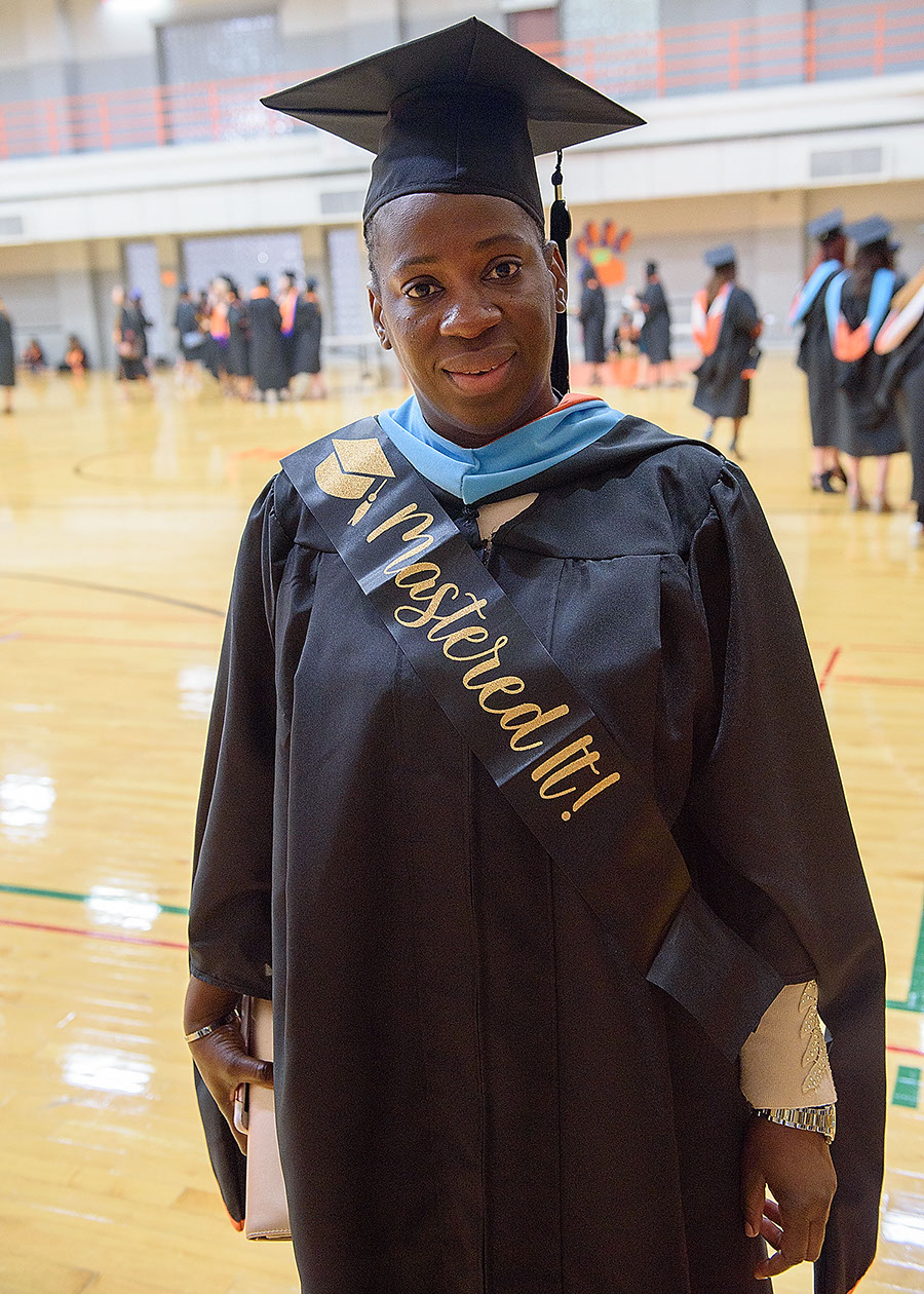 A woman wearing graduation garb also wears a sash that says Mastered It!