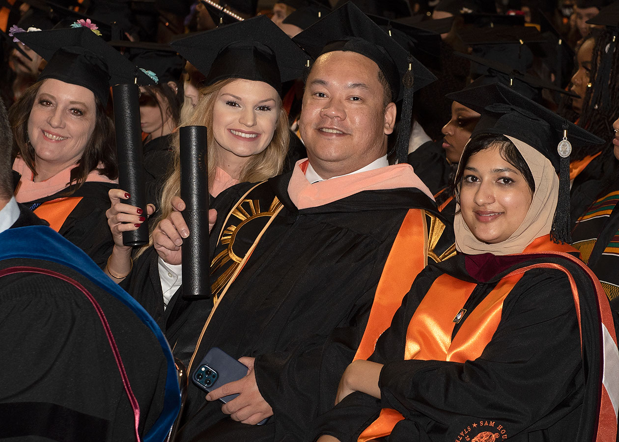 Graduates sitting in their chairs at commencement and smiling at the camera.