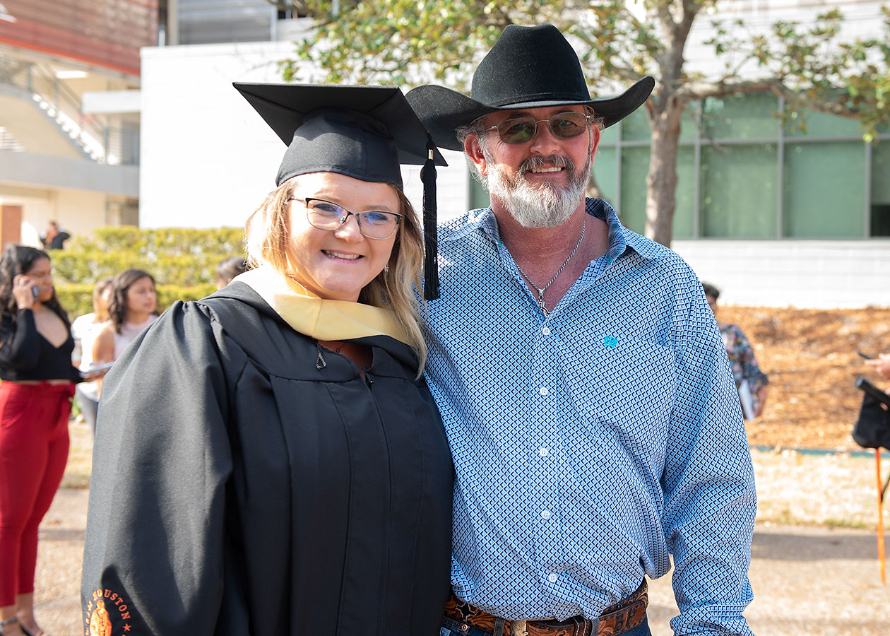 A graduate and a loved one embrace in front of a camera outside of Johnson Coliseum.