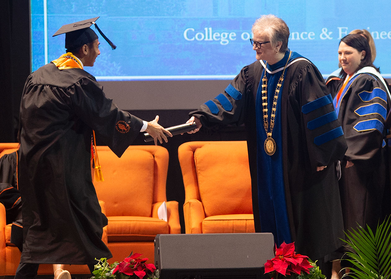 President Alisa White hands a degree tube to a graduate as he crosses the stage.