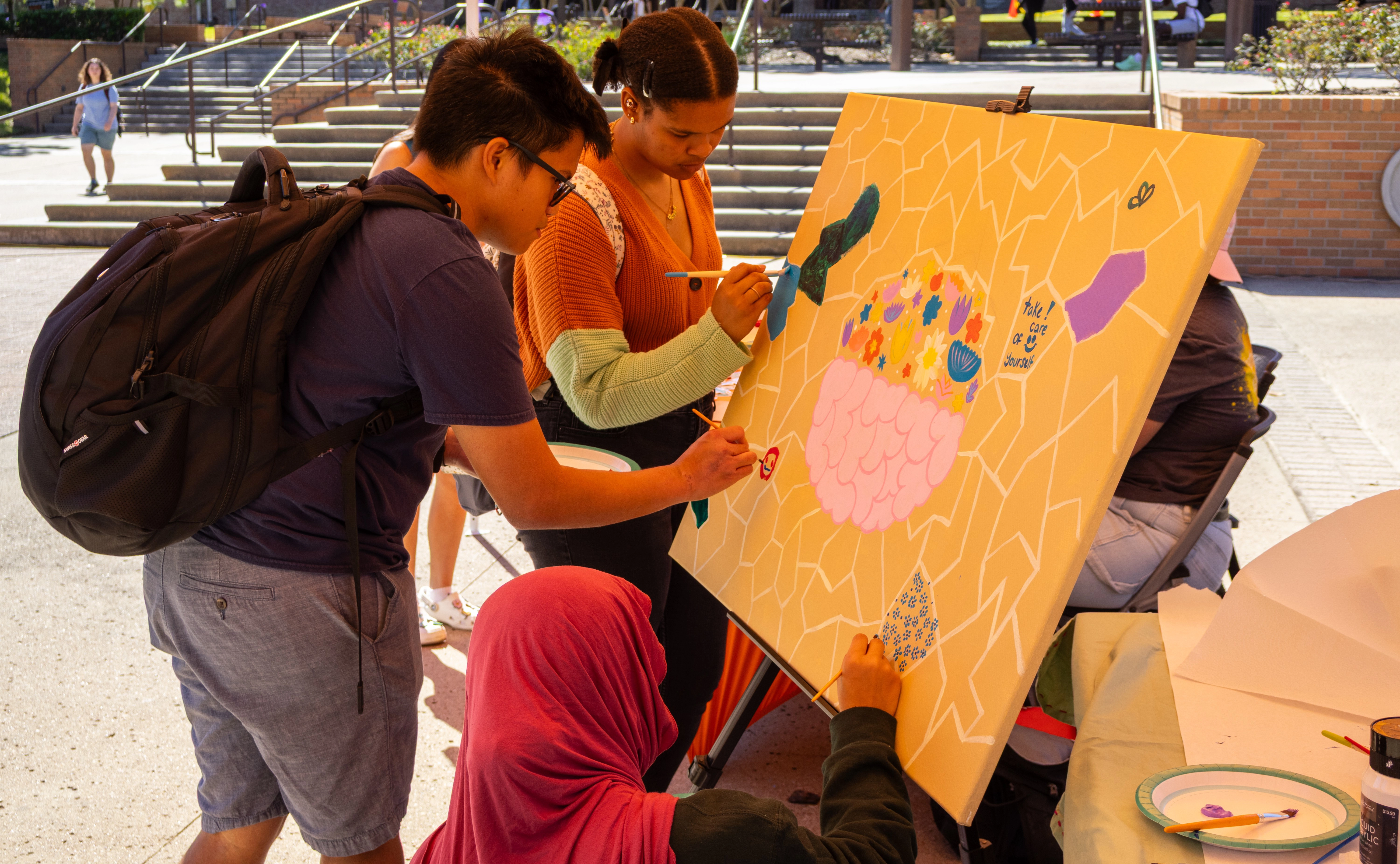 students gather together to paint canvas