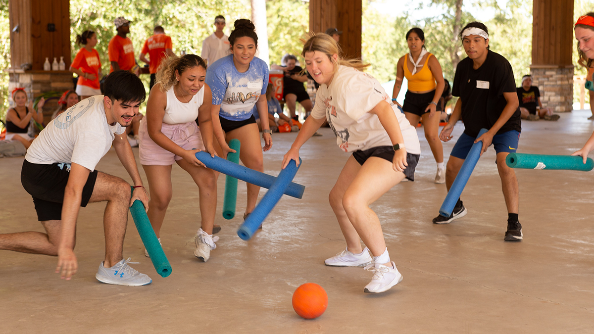 Students play a game with pool noodles and a ball.