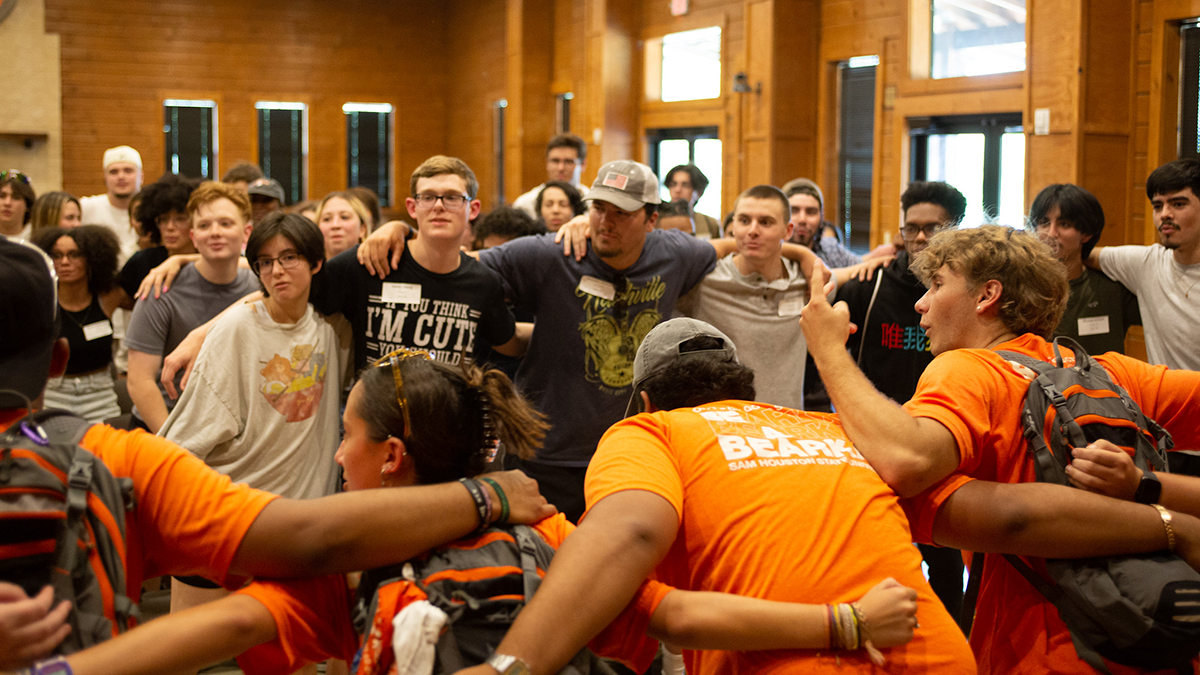 Students stand close together with their arms around one another's shoulders.