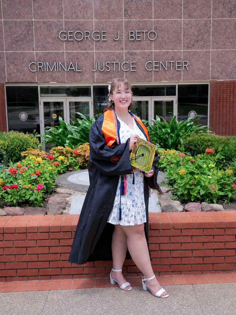 Emily Linklater, SHSU criminal justice Class of 2026, poses in graduation regalia holding her decorated cap in front of the George J. Beto Criminal Justice Center.