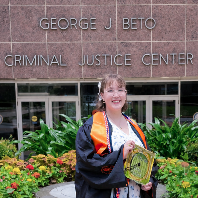 Emily Linklater, SHSU criminal justice Class of 2026, poses in graduation regalia holding her decorated cap in front of the George J. Beto Criminal Justice Center.