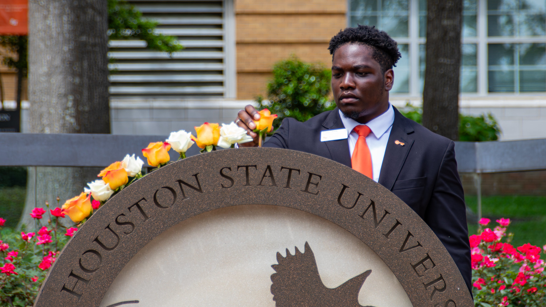SHSU Orange Key Ambassador adds an orange rose to the Raven's call statue.