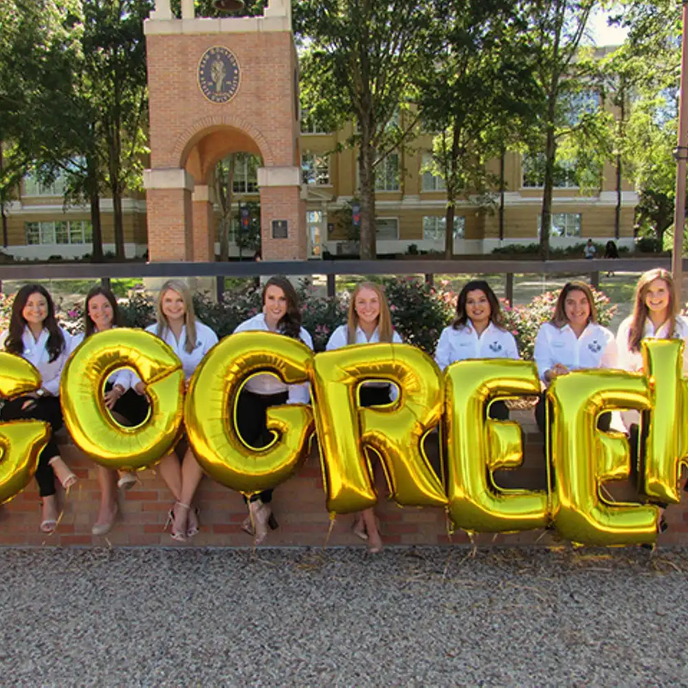 Students holding balloons that spell out, “Go Greek”
