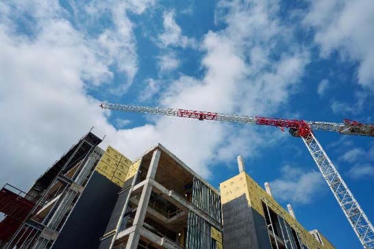 Construction crane over the future Health Professions Building, with exposed concrete and insulation panels against a blue sky.