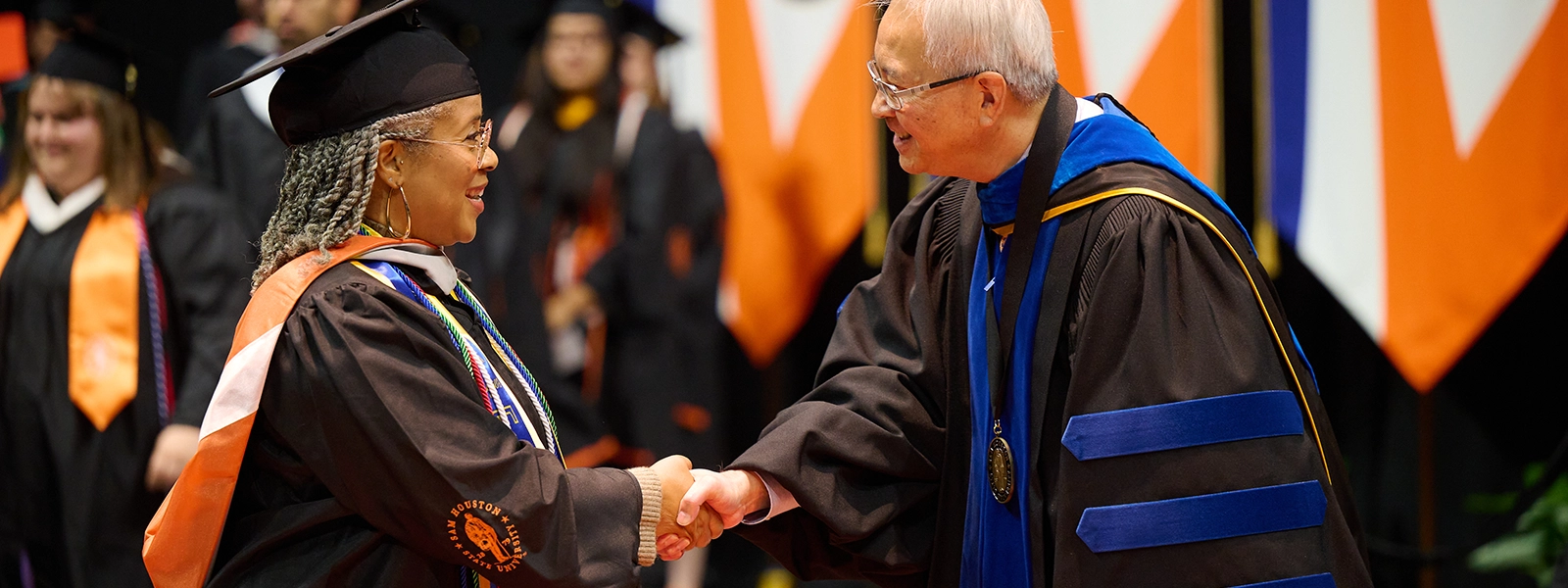 A graduate shaking hands with the dean as they walk across the commencement stage