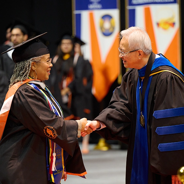 A graduate in a cap and gown shaking hands with a professor during a commencement ceremony