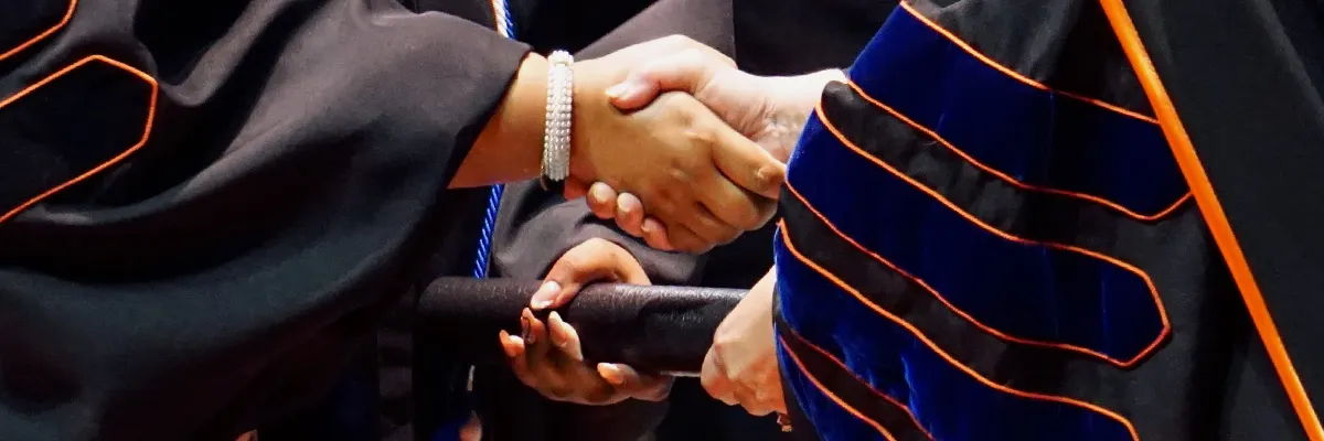 A graduate shaking hands with SHSU President White as they receive their degree