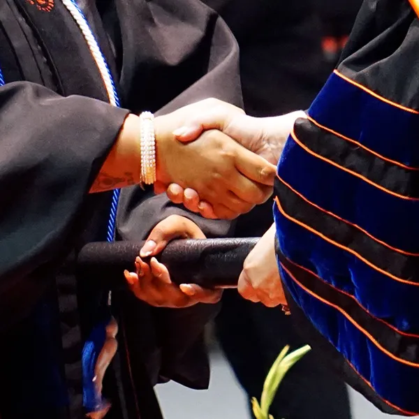 A graduate shaking hands with SHSU President White as they receive their degree