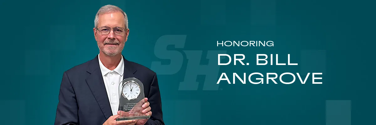 Dr. Bill Angrove smiles holding a glass clock award against a teal background