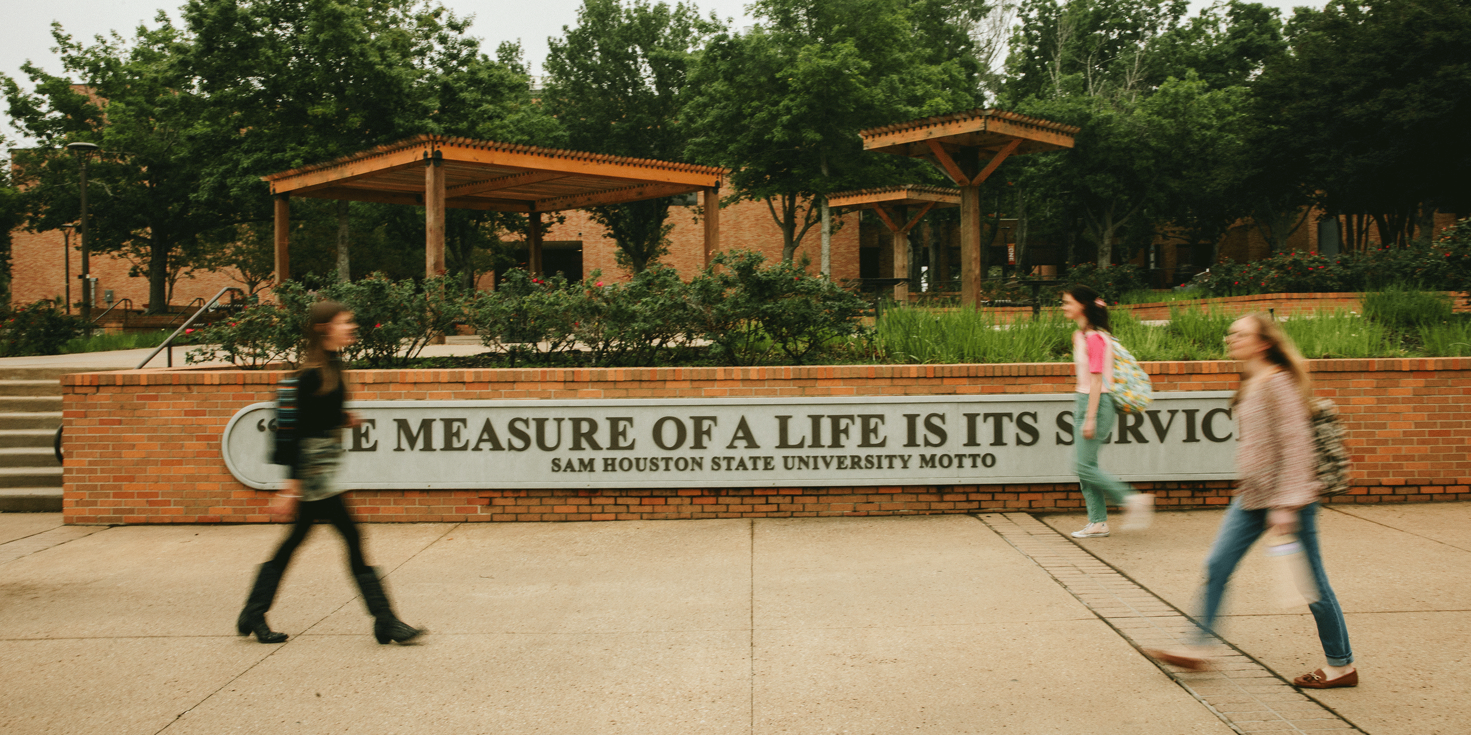 Students walking past a sign with the university motto: the measure of a life is its service