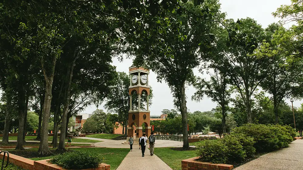 campus bell tower with 3 students walking