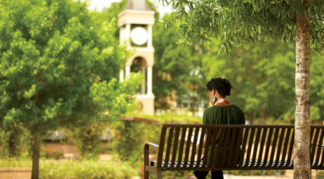 A student is sitting and thinking on a bench at Sam Houston State University in front of the clock tower.