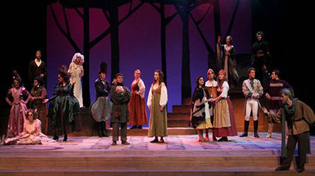 A group of students are putting on a play in period costume on a stage.