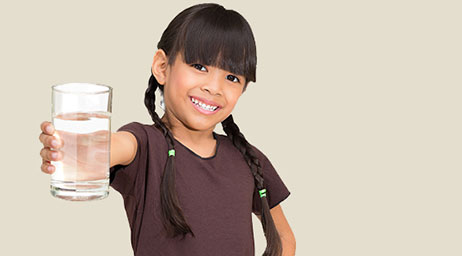 A smiling child holds out a glass of water.