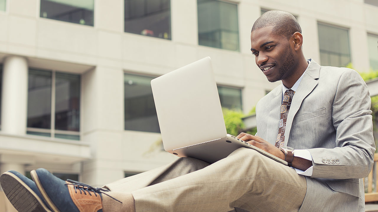 Professionally dressed man working on a laptop outside