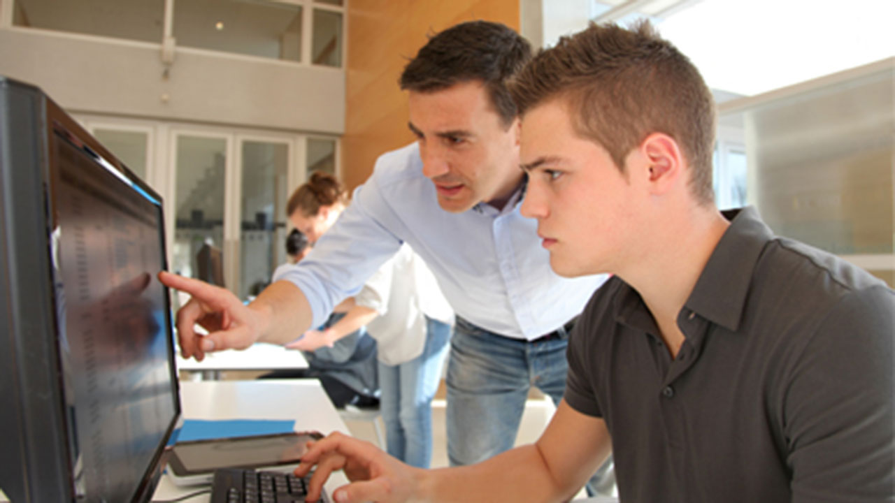 Teacher helping a student working on their computer in the classroom.