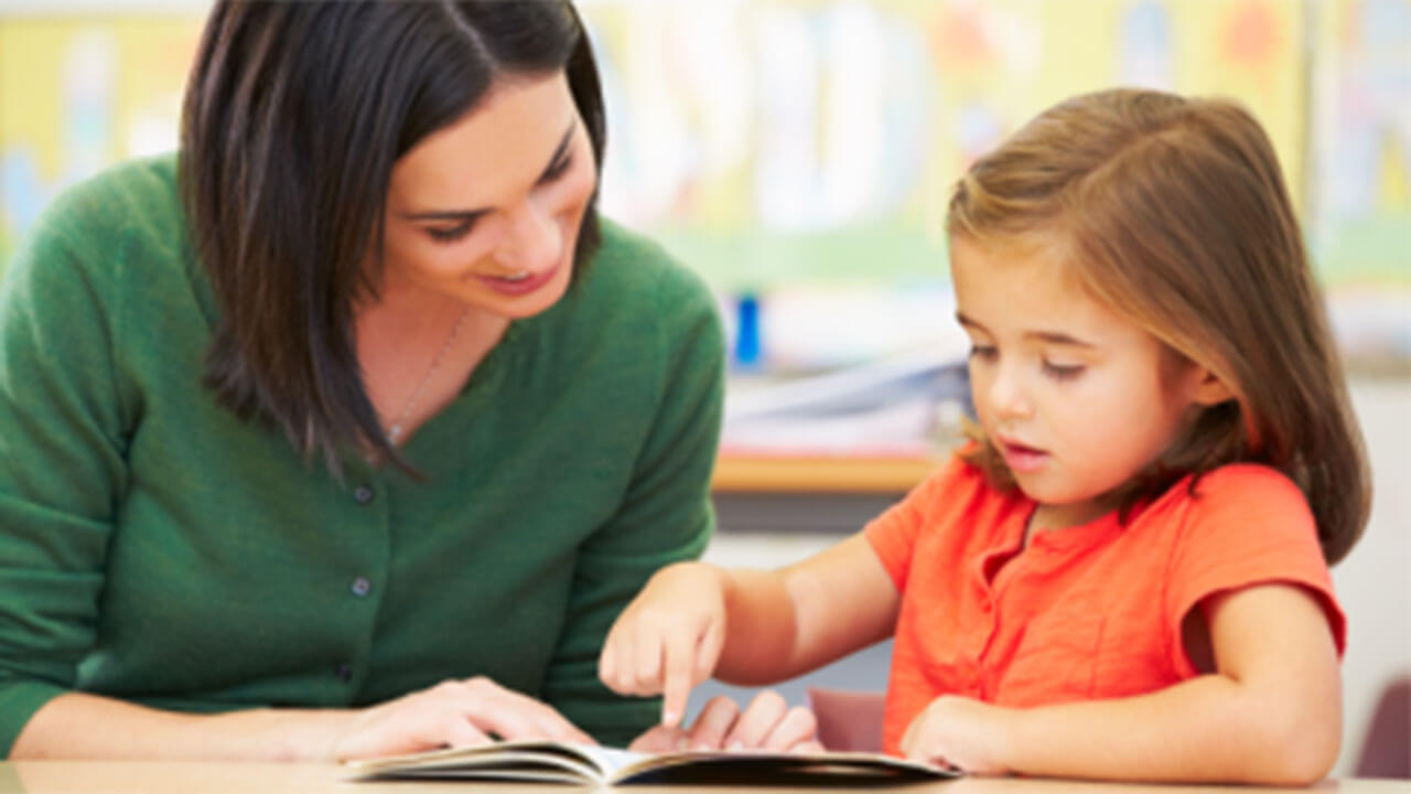 Teacher helping a young girl to read a book