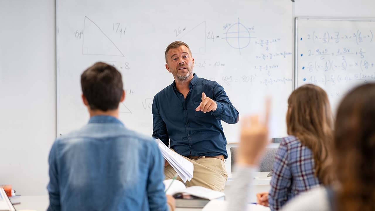 A teacher in front of a whiteboard and students.