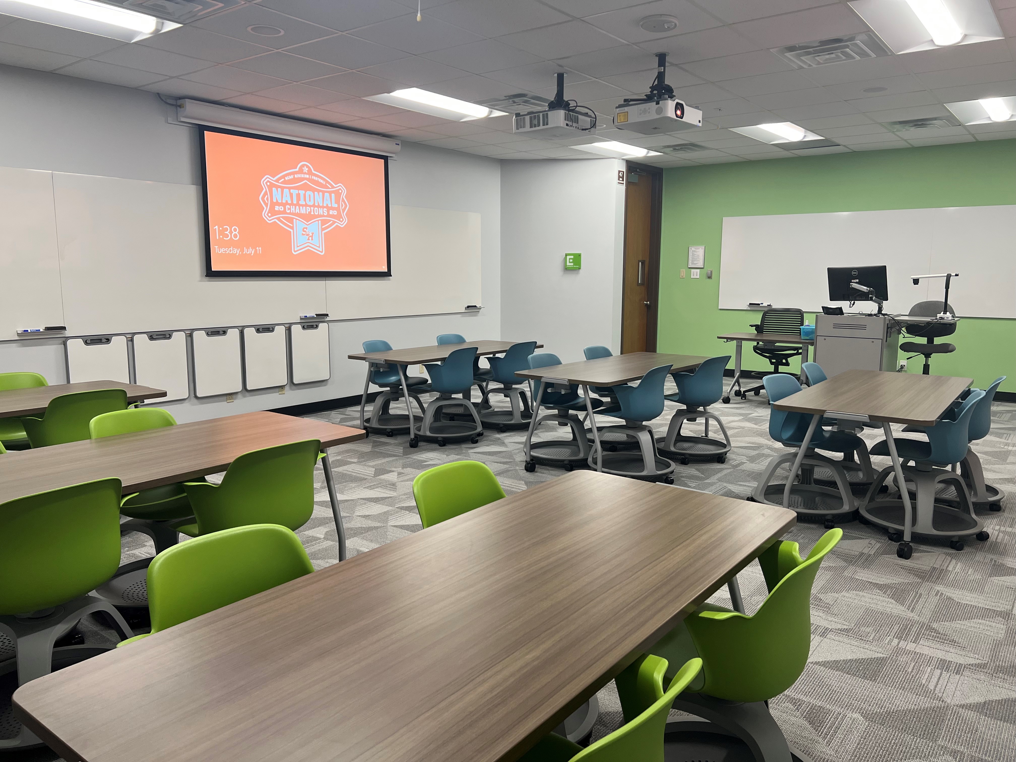 LDB 208, tables and chairs in a classroom with a projector screen in the background.