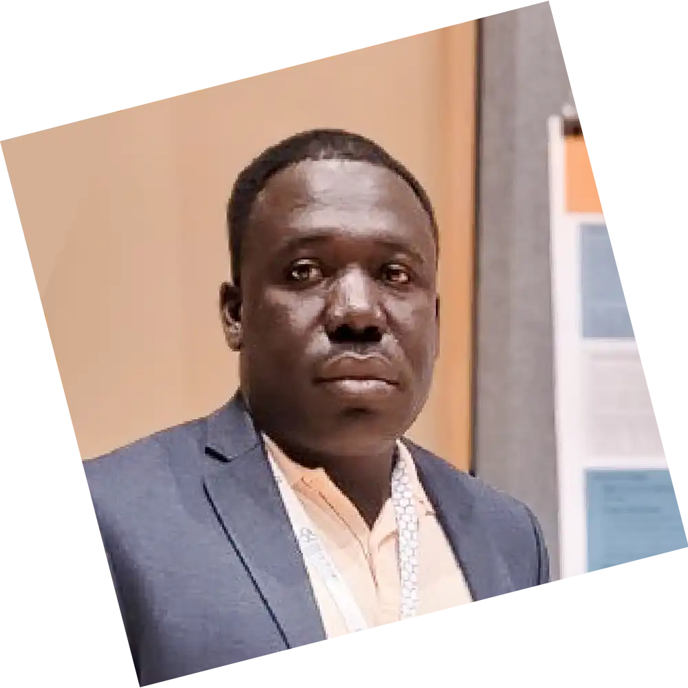 Person wearing a suit jacket and light-colored shirt standing indoors near a display board with documents and charts.