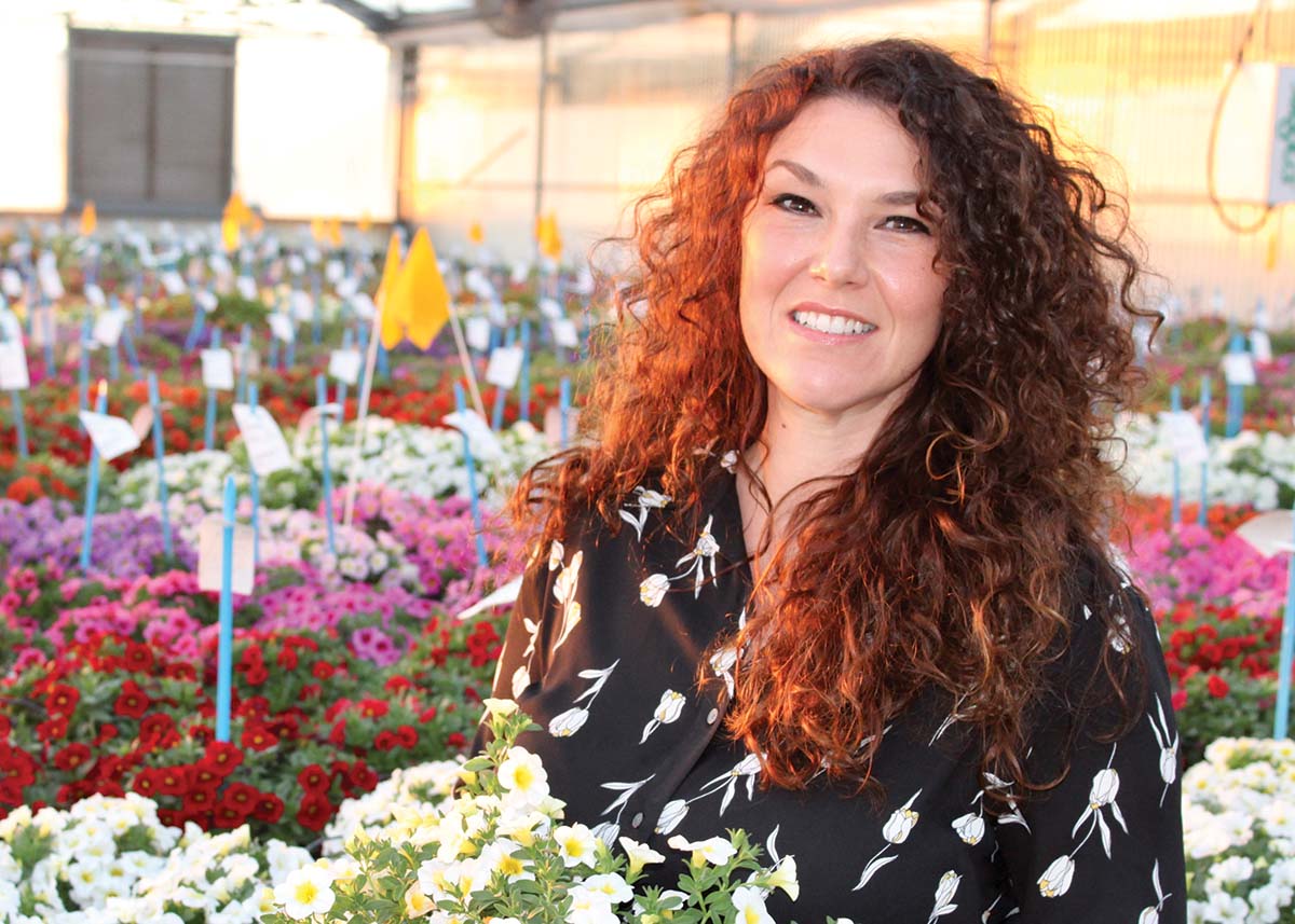 Laura Masor poses in a greenhouse full of colorful flowers.