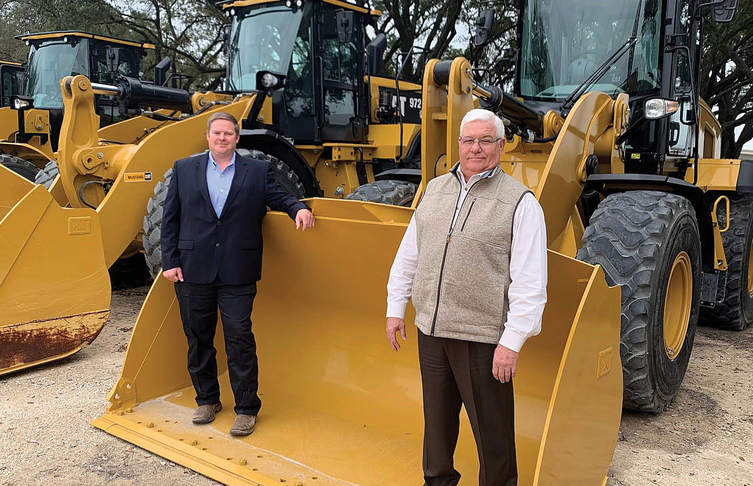 Dyke Rasco and Scott Weaver stand in the bucket of a CAT bulldozer.