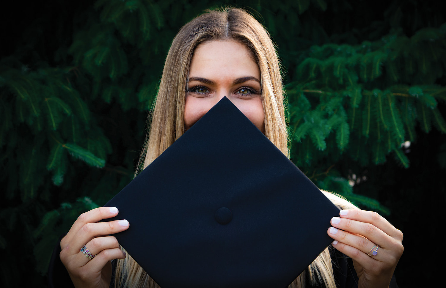 A woman holding up her graduate cap in front of her face.