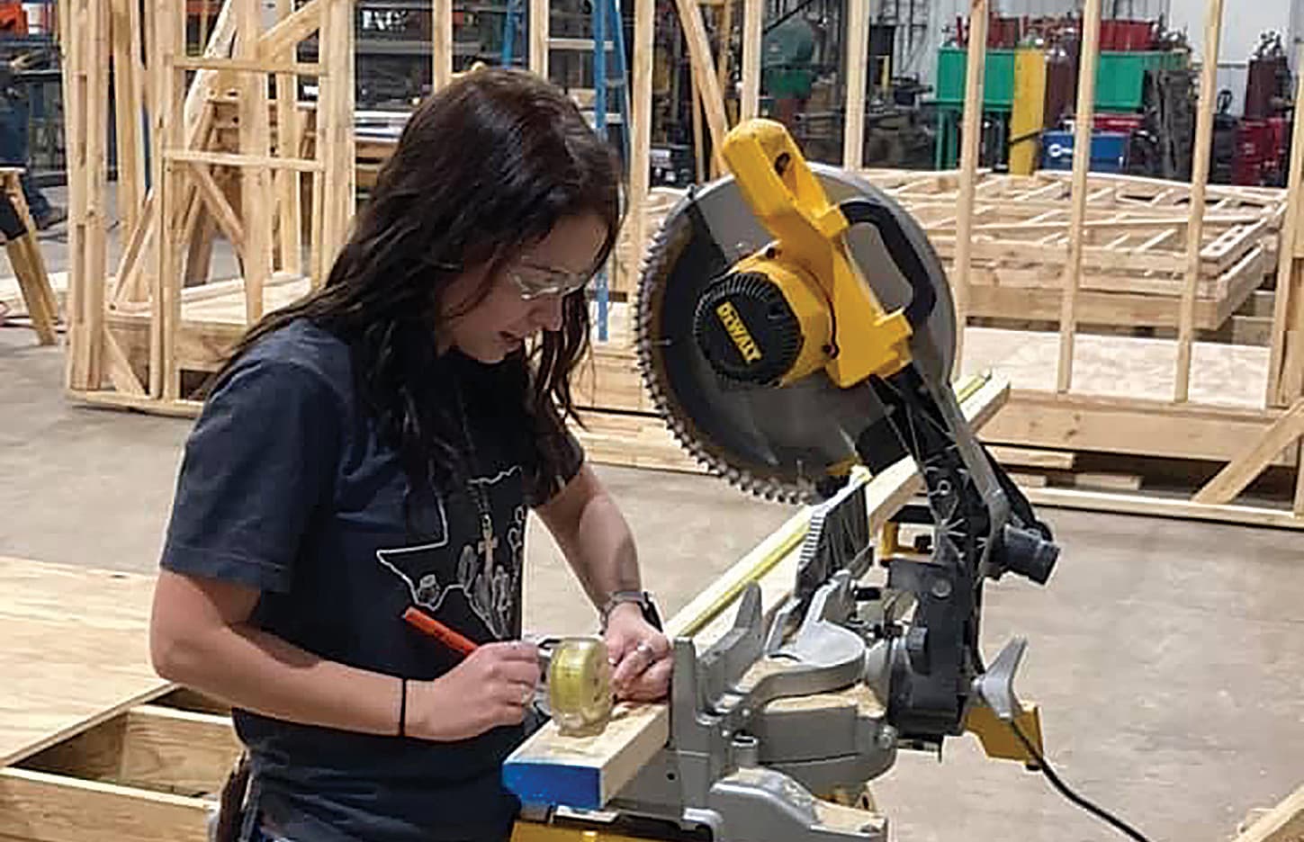 Cara Hooper marks a piece of lumber with a pencil before cutting it with a saw.