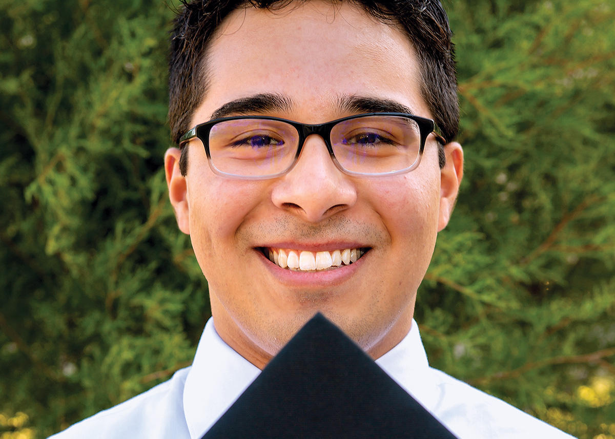 Jesus Martinez holds a graduation cap in front of his face.