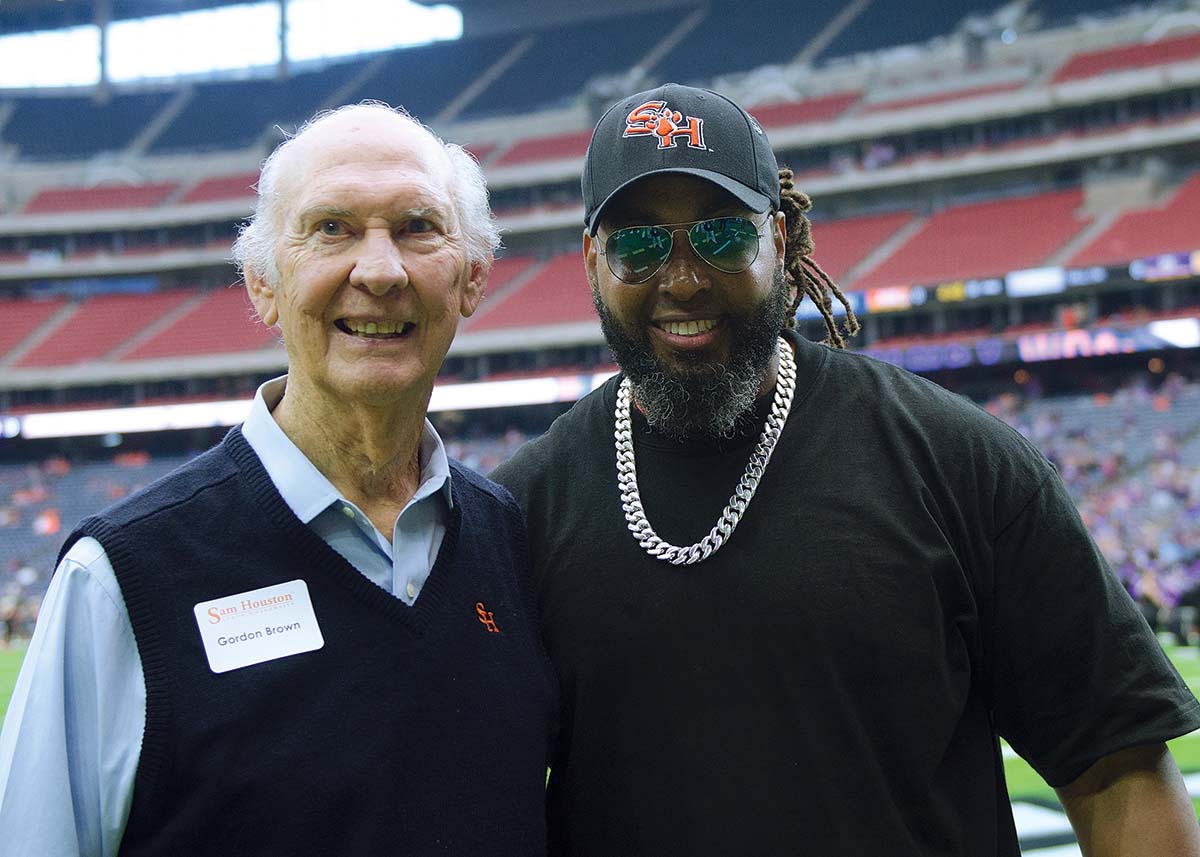 Gordon Brown posing with a football coach on the football field.