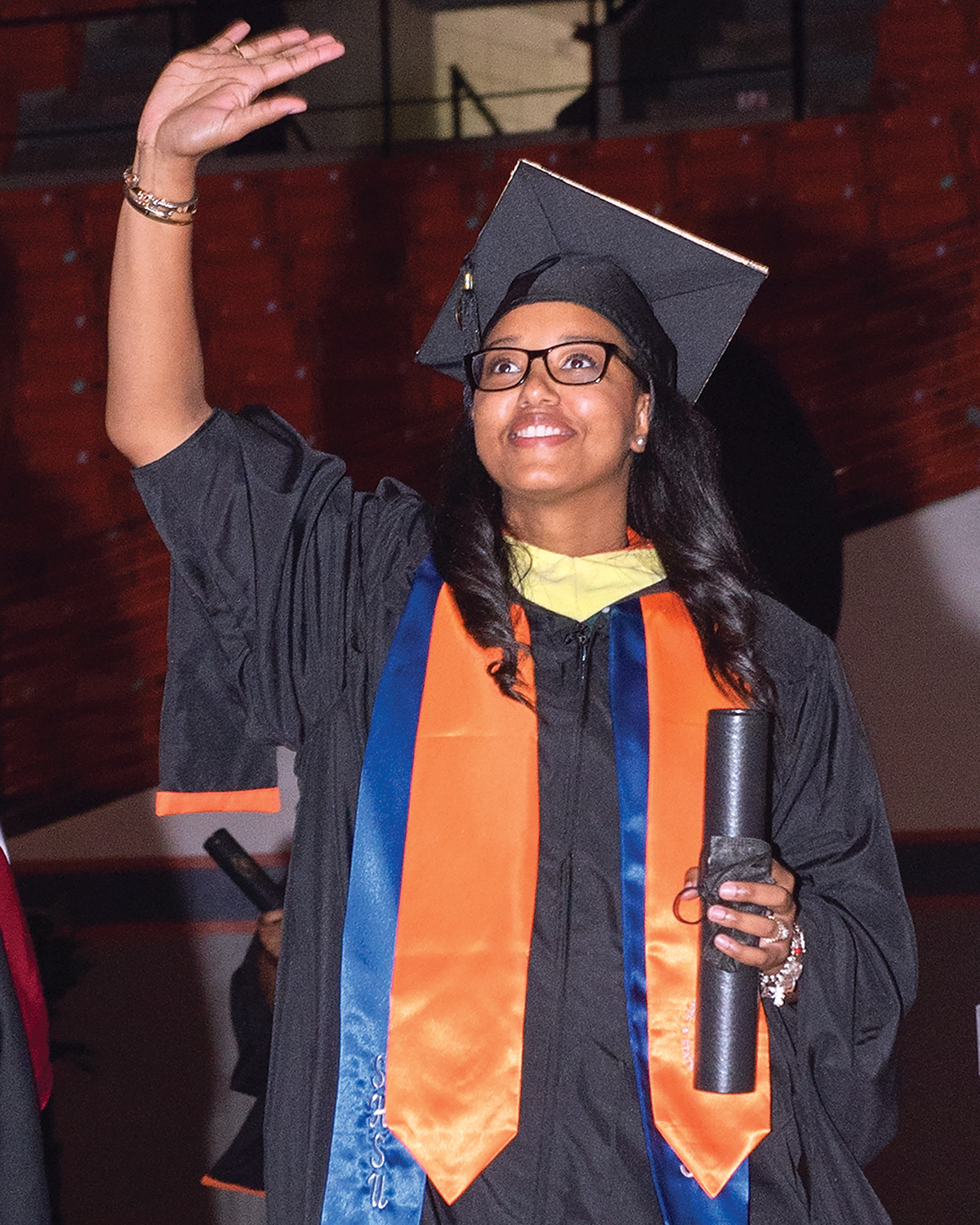 A student waves to the audience as she crosses the stage with her degree.