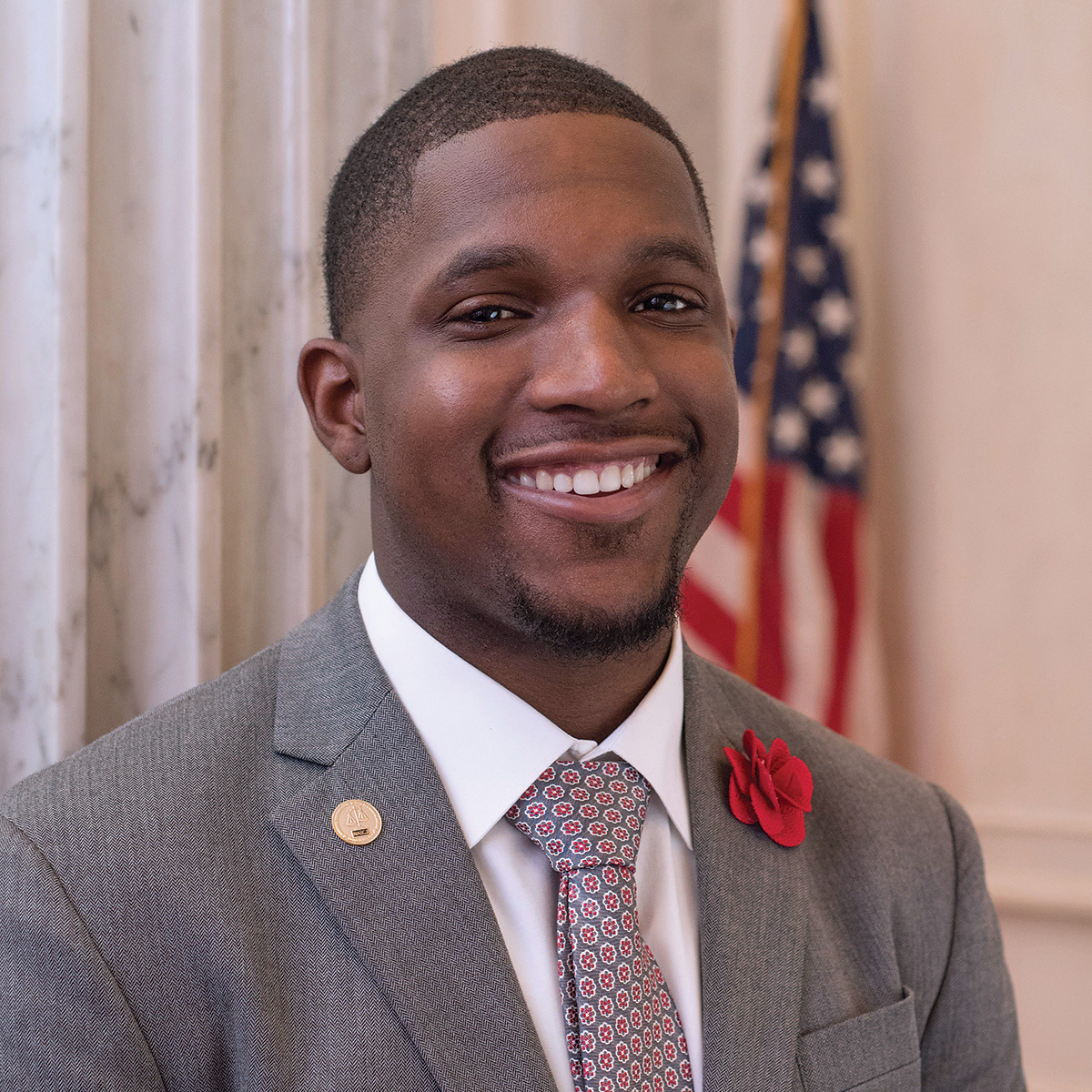 Alvin Casimere smiles with strong marble walls and an American flag in the background.