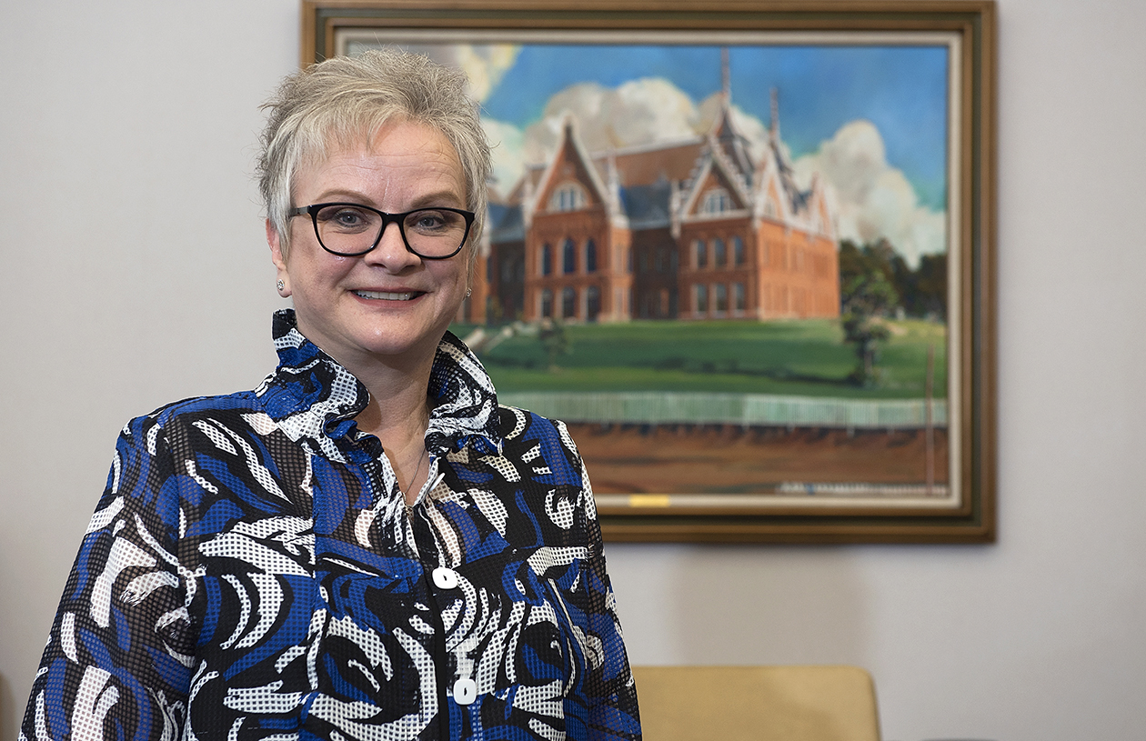 SHSU President Alisa White smiles for the camera in front of a painting of Old Main.