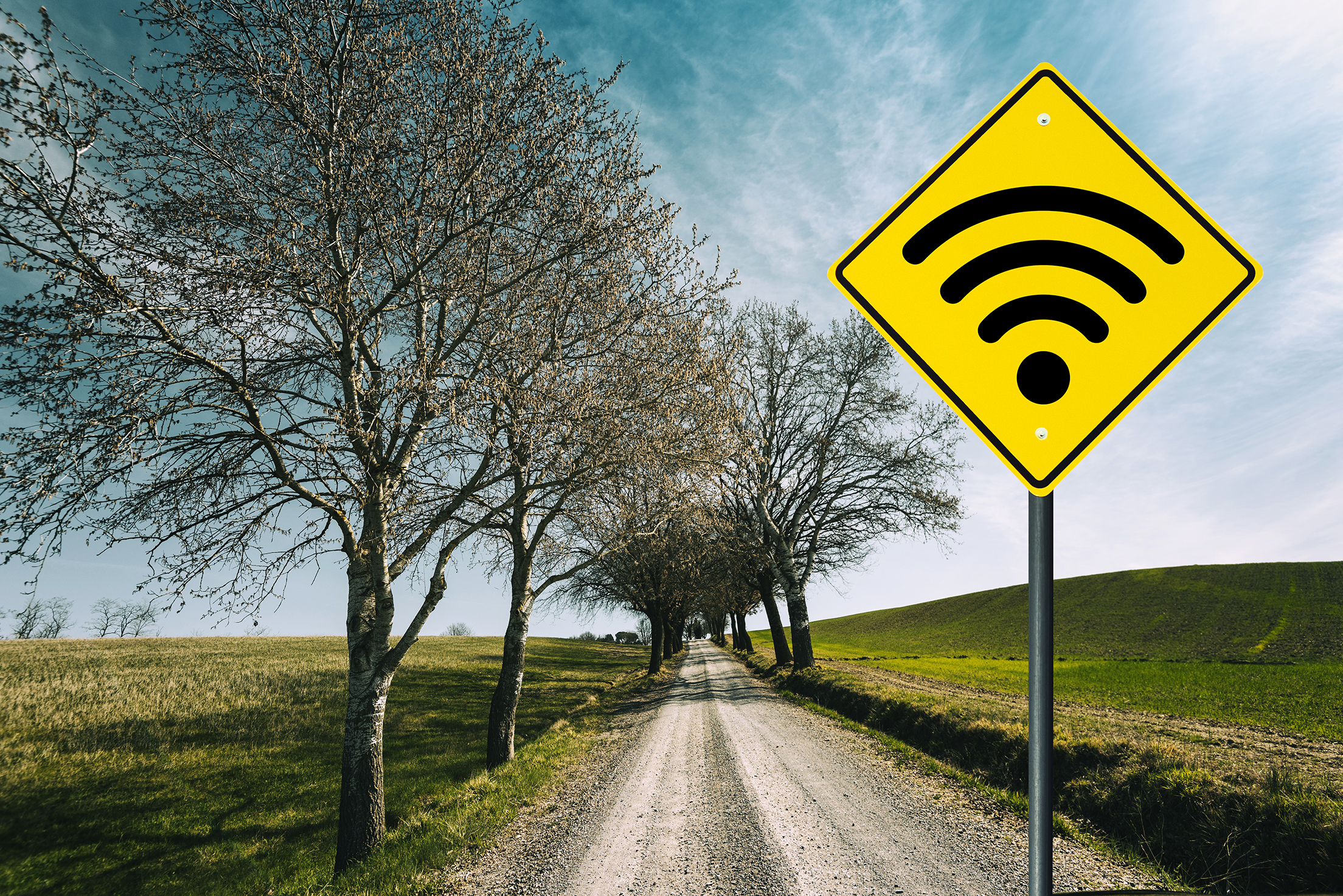 A rural road with a yellow road sign featuring a Wifi signal symbol.