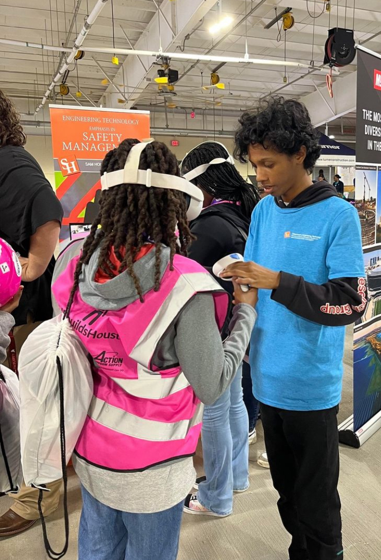 Yannis Lagrosa helps a student from SHEBuildsHouston use a VR headset.